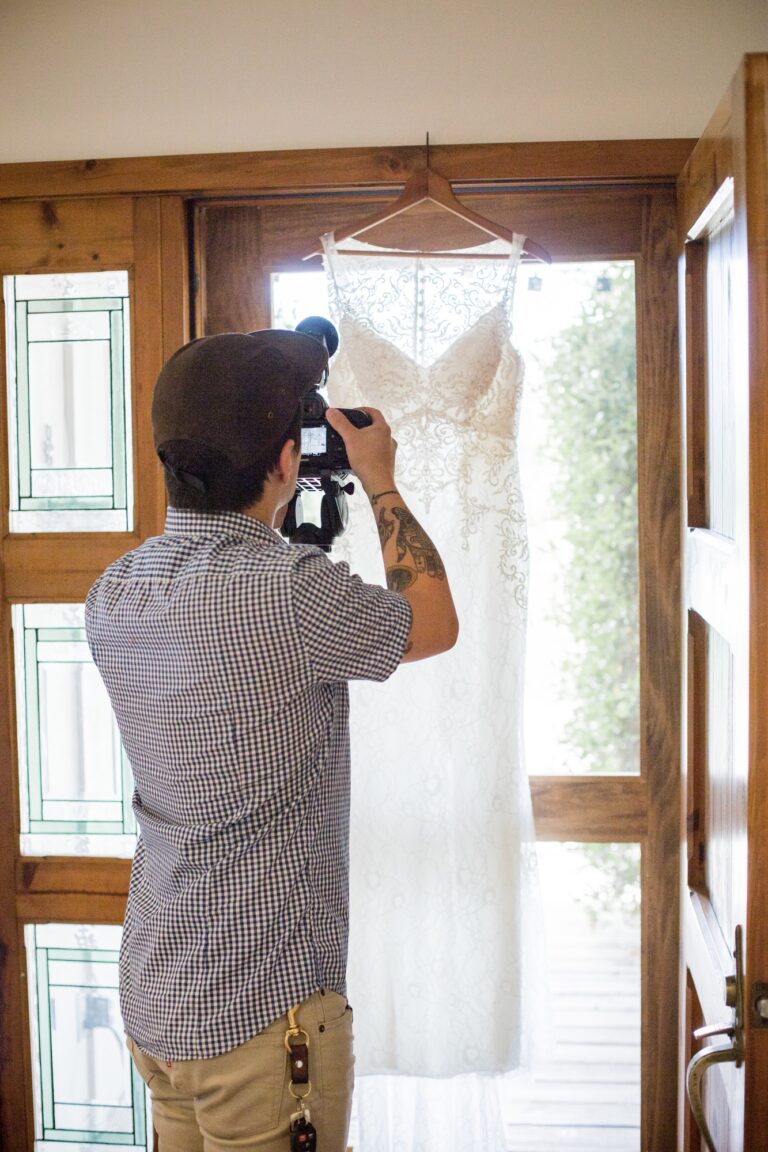 A young videographer shoots a beautiful wedding gown hanging in a doorway
